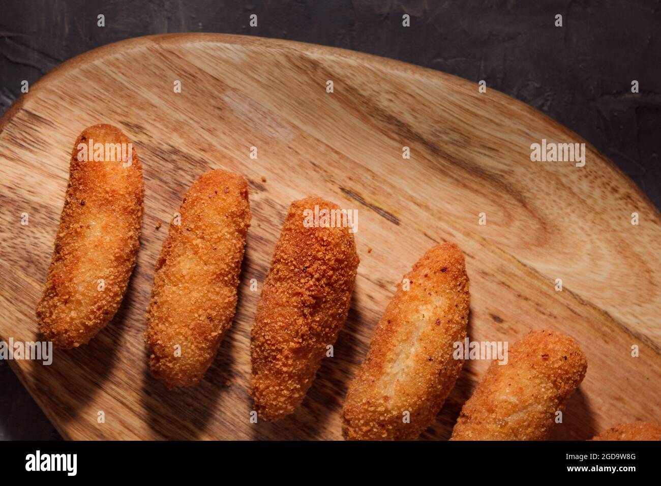 Hausgemachte traditionelle spanische Kroketten auf einem Holzbrett und schwarzem Hintergrund. Tapas. Dunkles Essen. Stockfoto