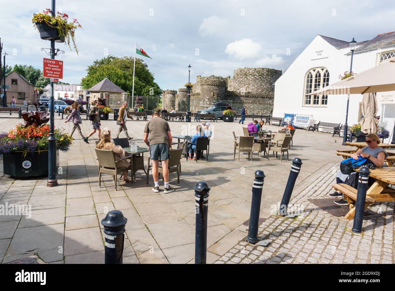 Menschen genießen die Sonne auf dem Schlossplatz in Beaumaris Anglesey mit dem alten Hofhaus und dem Schloss Beaumaris im Hintergrund Stockfoto