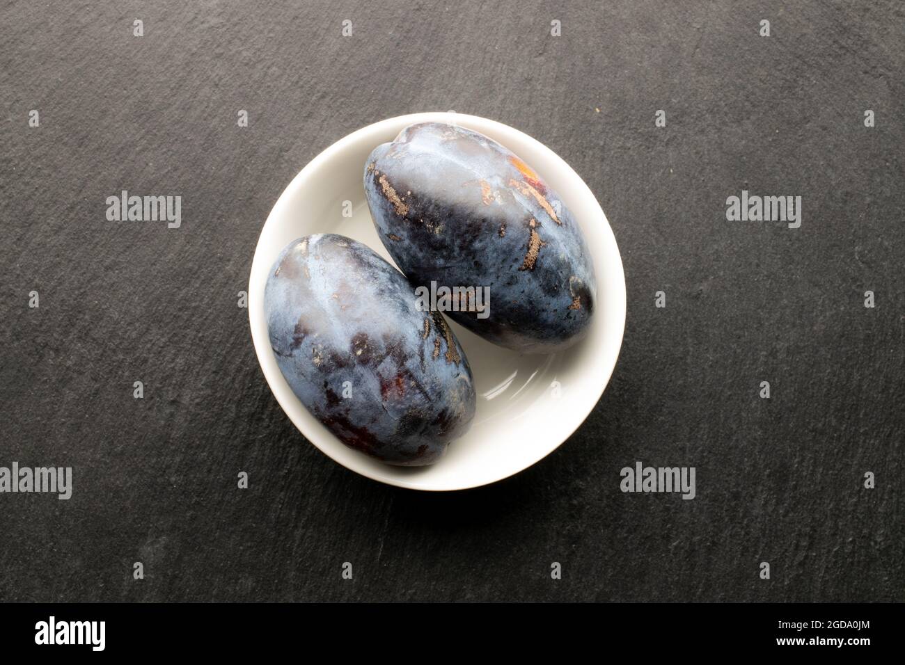 Zwei saftige dunkelviolette Pflaumen, Nahaufnahme, auf einem Schiefertafel, Draufsicht. Stockfoto