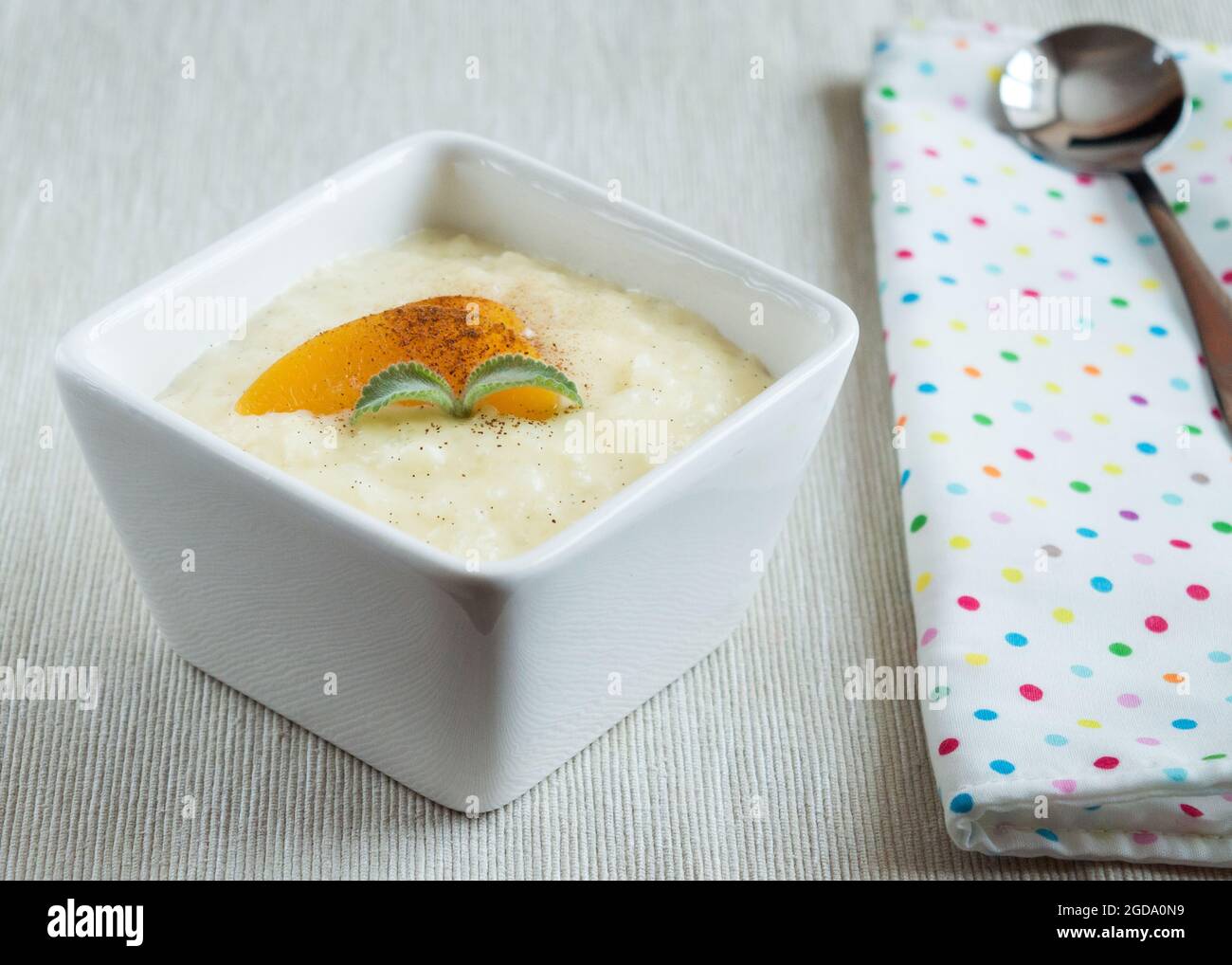 Reispudding in einer kleinen Schüssel, garniert mit Pfirsich und Minze. Stockfoto