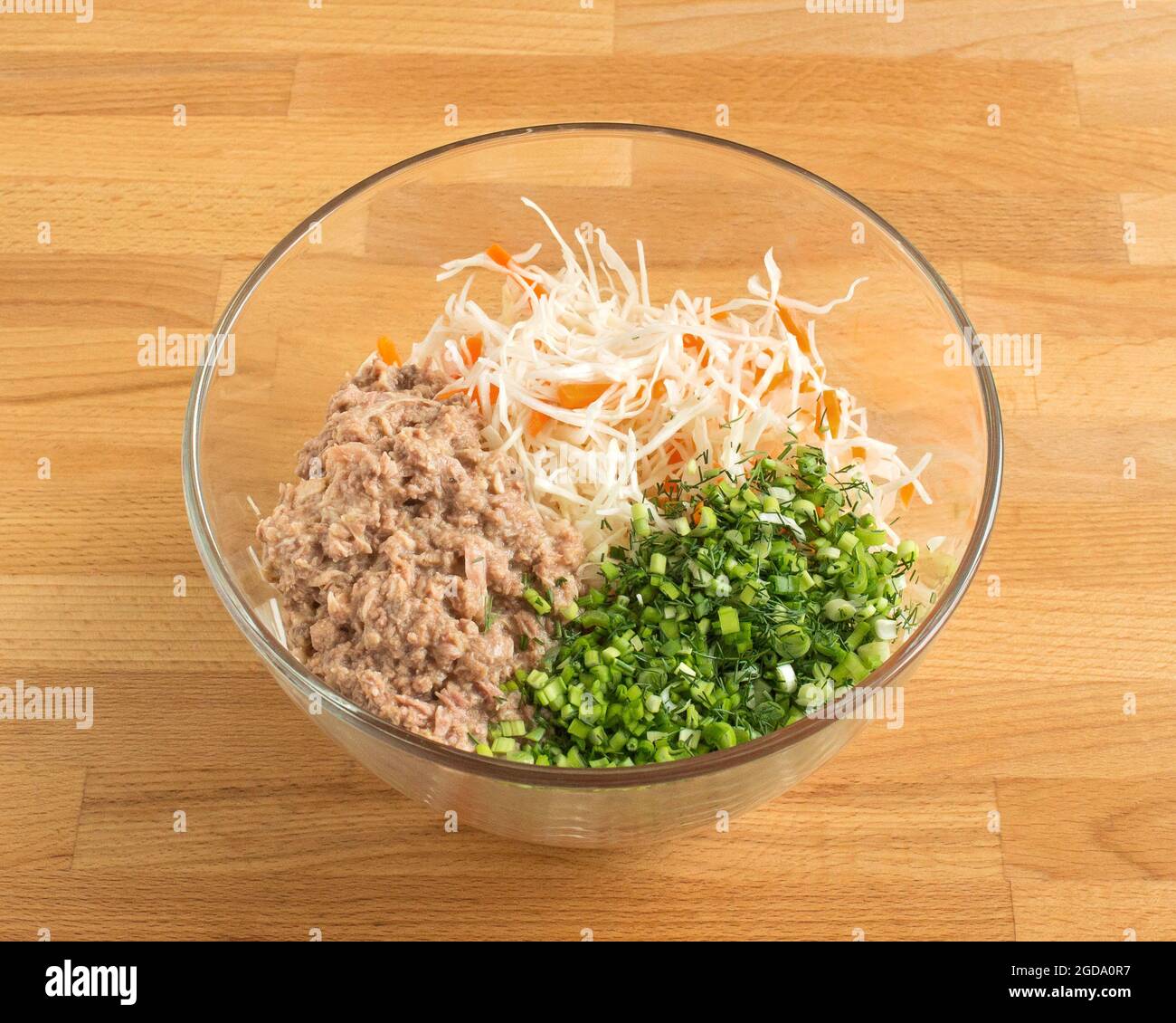 Zutaten in einer transparenten Fischsalatschüssel. Konserven, gehackte grüne Zwiebeln, frischer Kohl. Stockfoto
