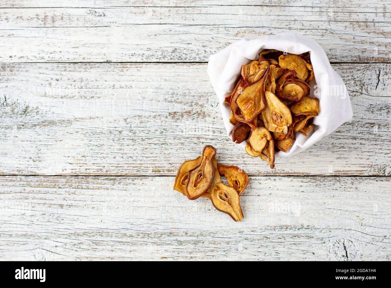 Ein Haufen getrockneter Birnenscheiben in weißem Beutel auf Holzgrund. Getrocknete Fruchtchips. Gesundes veganes Essen Stockfoto