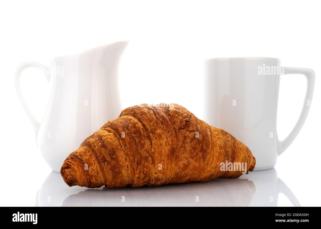 Ein frisch gebackenes duftendes Croissant mit weißem Milchkännchen und Tasse, Nahaufnahme, isoliert auf Weiß. Stockfoto
