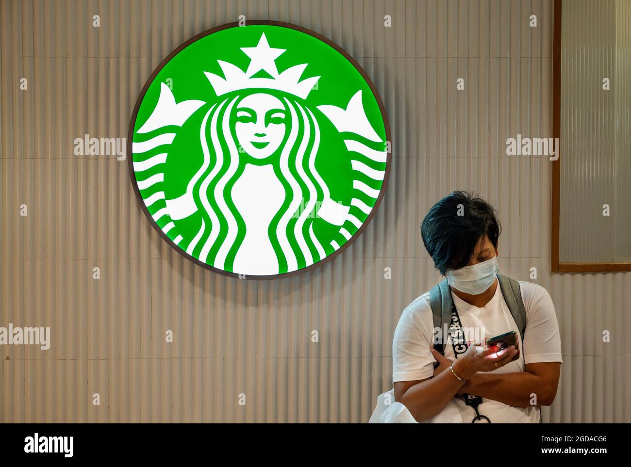 Ein Shopper nutzt sein Smartphone neben der amerikanischen multinationalen Kette, dem Starbucks Coffee-Logo und dem Store in Hongkong. Stockfoto