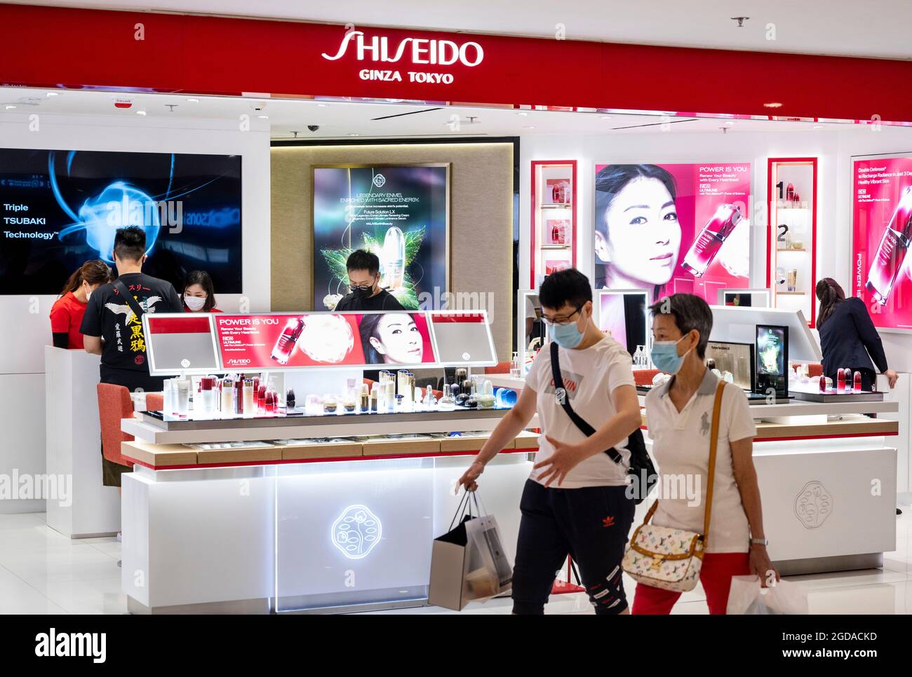 Käufer mit Gesichtsmasken kommen am japanischen, multinationalen Körperpflegeunternehmen Shiseido-Laden vorbei, der in Hongkong zu sehen ist. Stockfoto