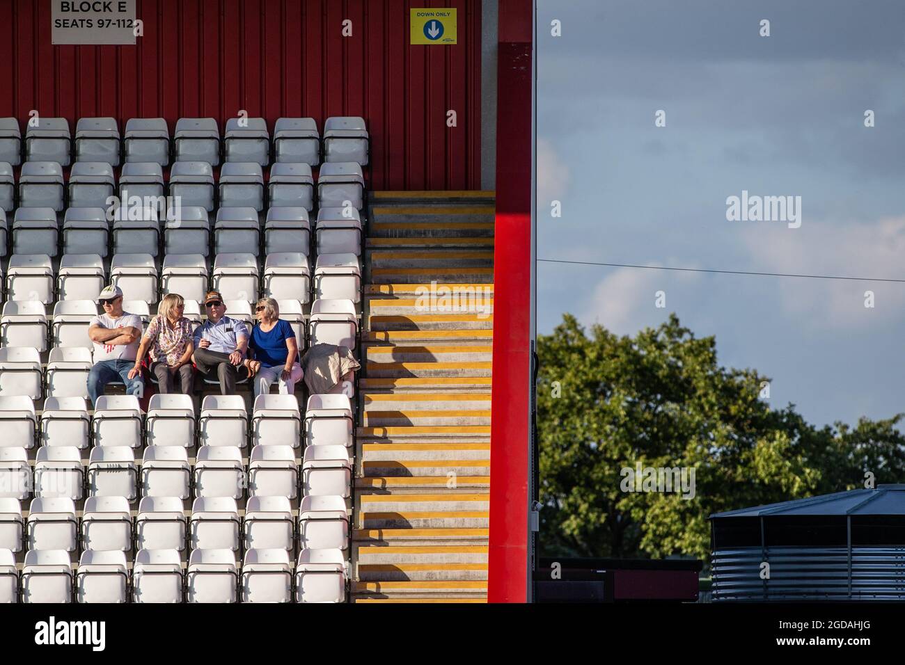 Kleine Gruppe von Fußballzuschauern, die isoliert auf Sitzen im Fußballstadion sitzen Stockfoto