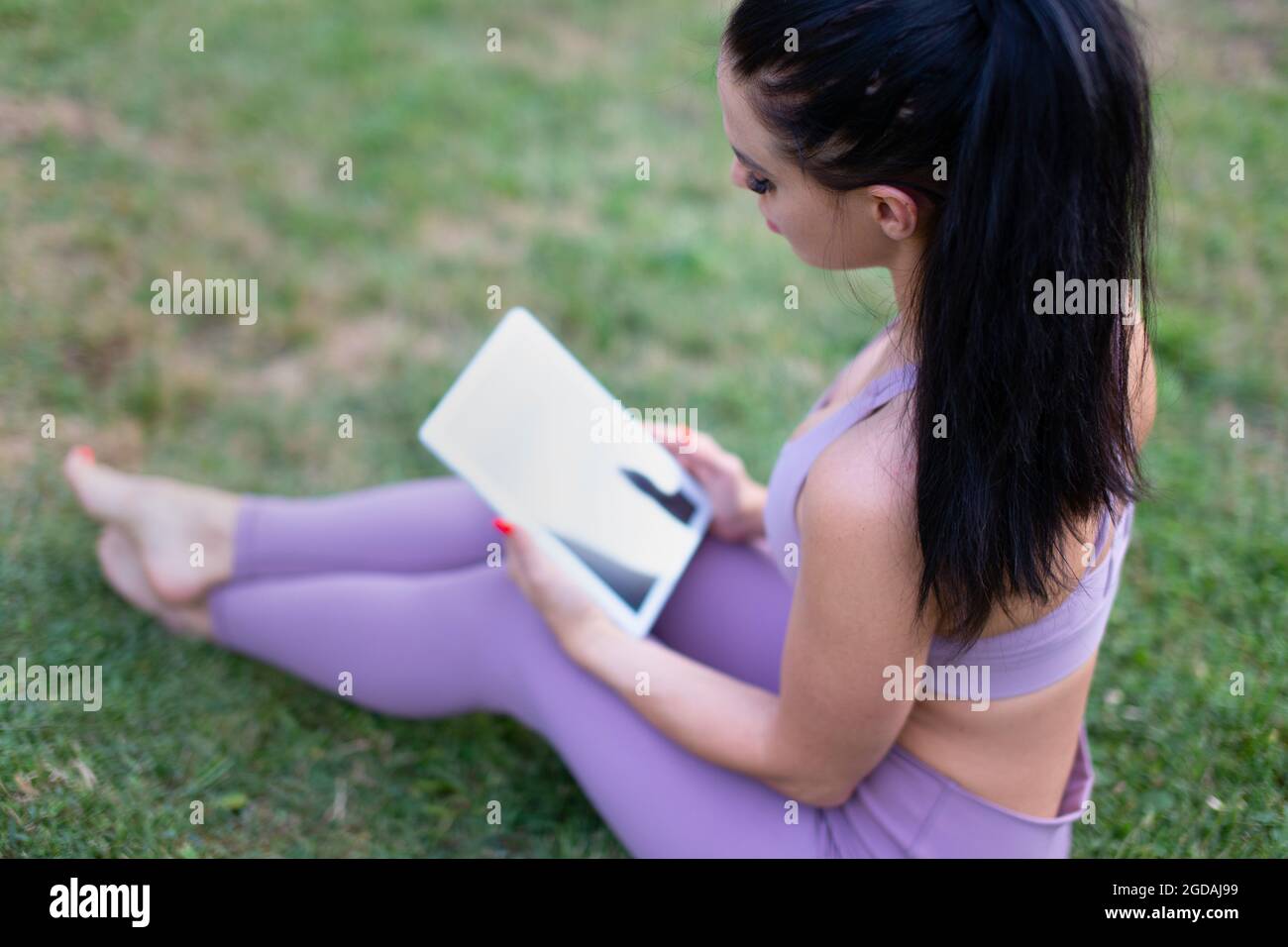 Junge Frau in Sportbekleidung mit digitalem Tablet, sitzend auf Gras Stockfoto