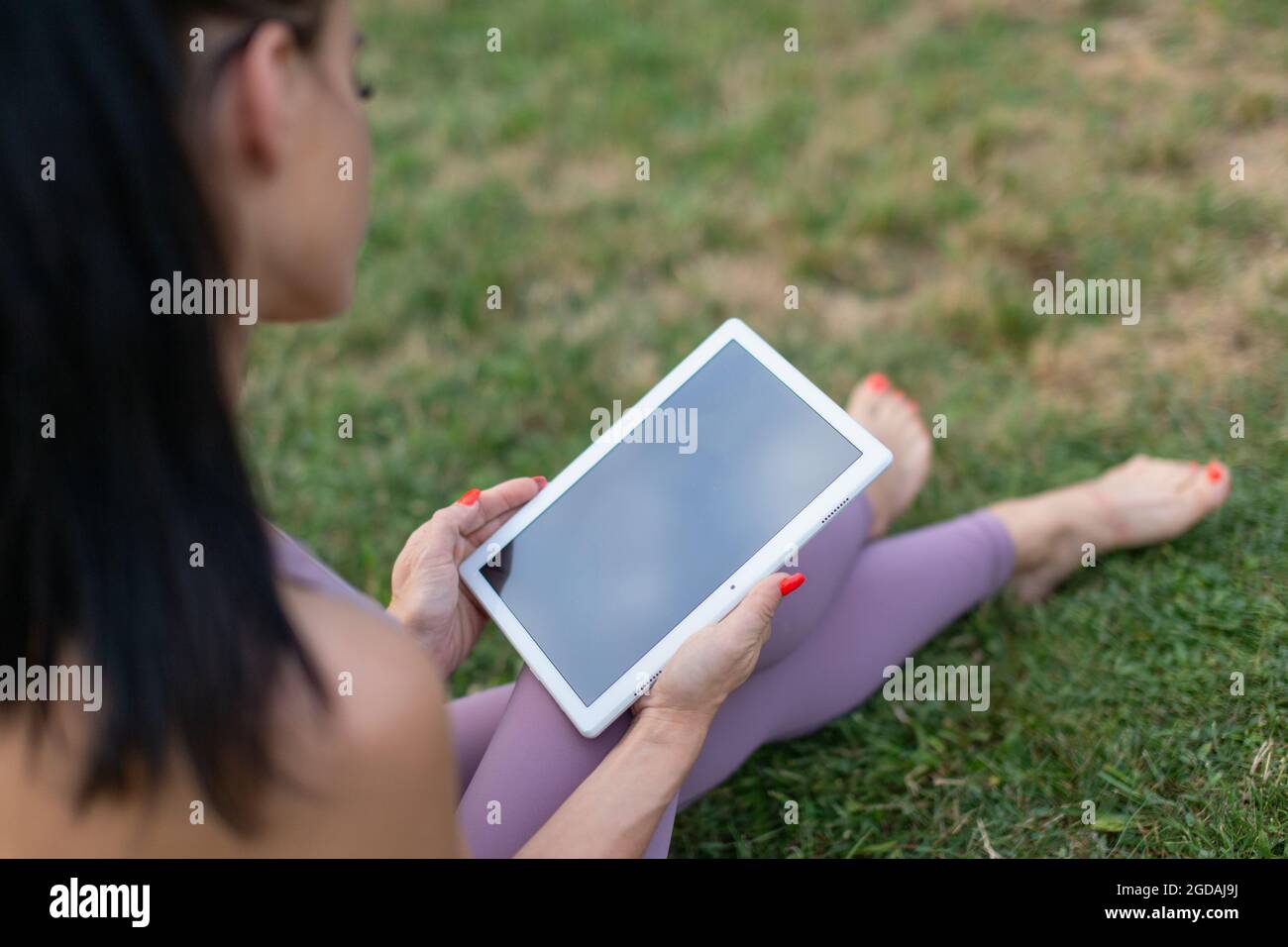 Junge Frau in Sportbekleidung mit digitalem Tablet aus der Nähe, sitzt auf Gras Stockfoto