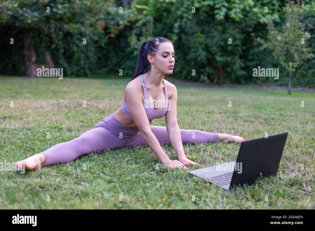 Junge Frau in Sportbekleidung Lernen aus Tutorial-Video Splitting Pose im Garten, im Freien Stockfoto
