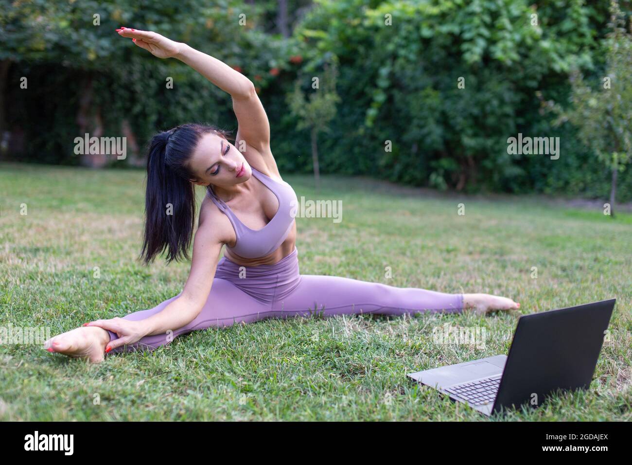 Junge Frau in Sportbekleidung lernen von Tutorial-Video Stretching im Garten, im Freien Stockfoto