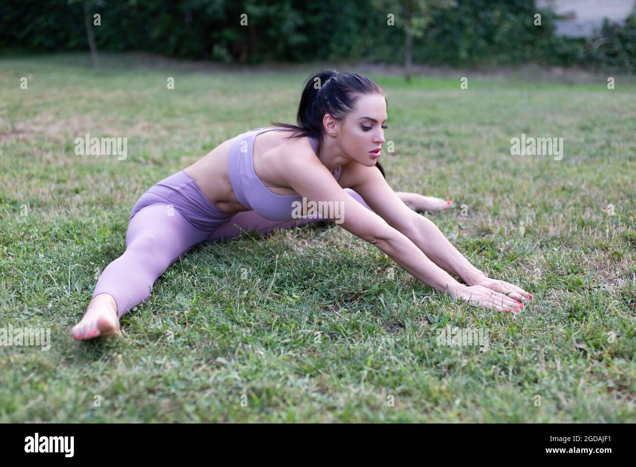 Junge kaukasische Frau in Sportbekleidung Stretching im Garten auf Gras, im Freien Stockfoto