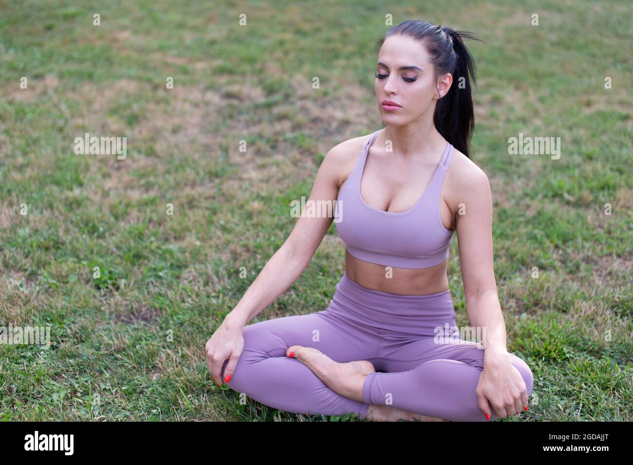 Junge Frau im Yoga-Lotus sitzt meditierend im Garten Stockfoto