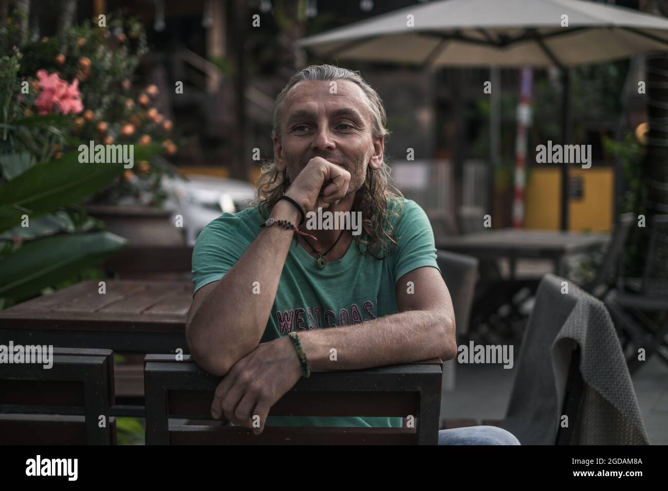 Porträt eines reifen, gutaussehenden Mannes, der auf der Sommerverande des Restaurants sitzt und seine Hand bis zum Kinn hält. Lange graue Haare. Hochwertige Fotos Stockfoto