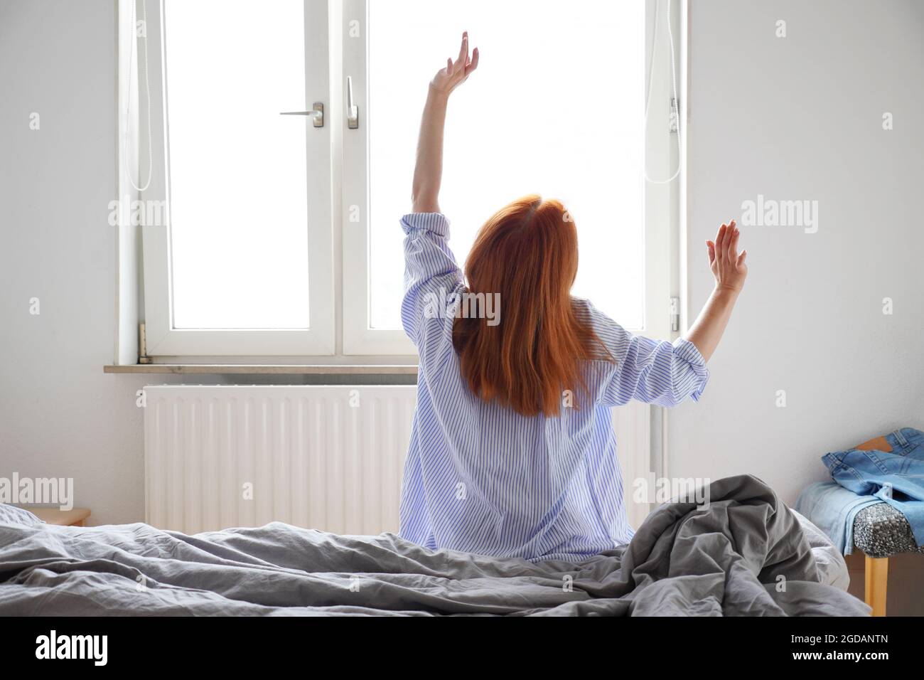 Junge Frau, die sich nach dem Aufwachen und dem Aufstehen aus dem Bett streckt Stockfoto
