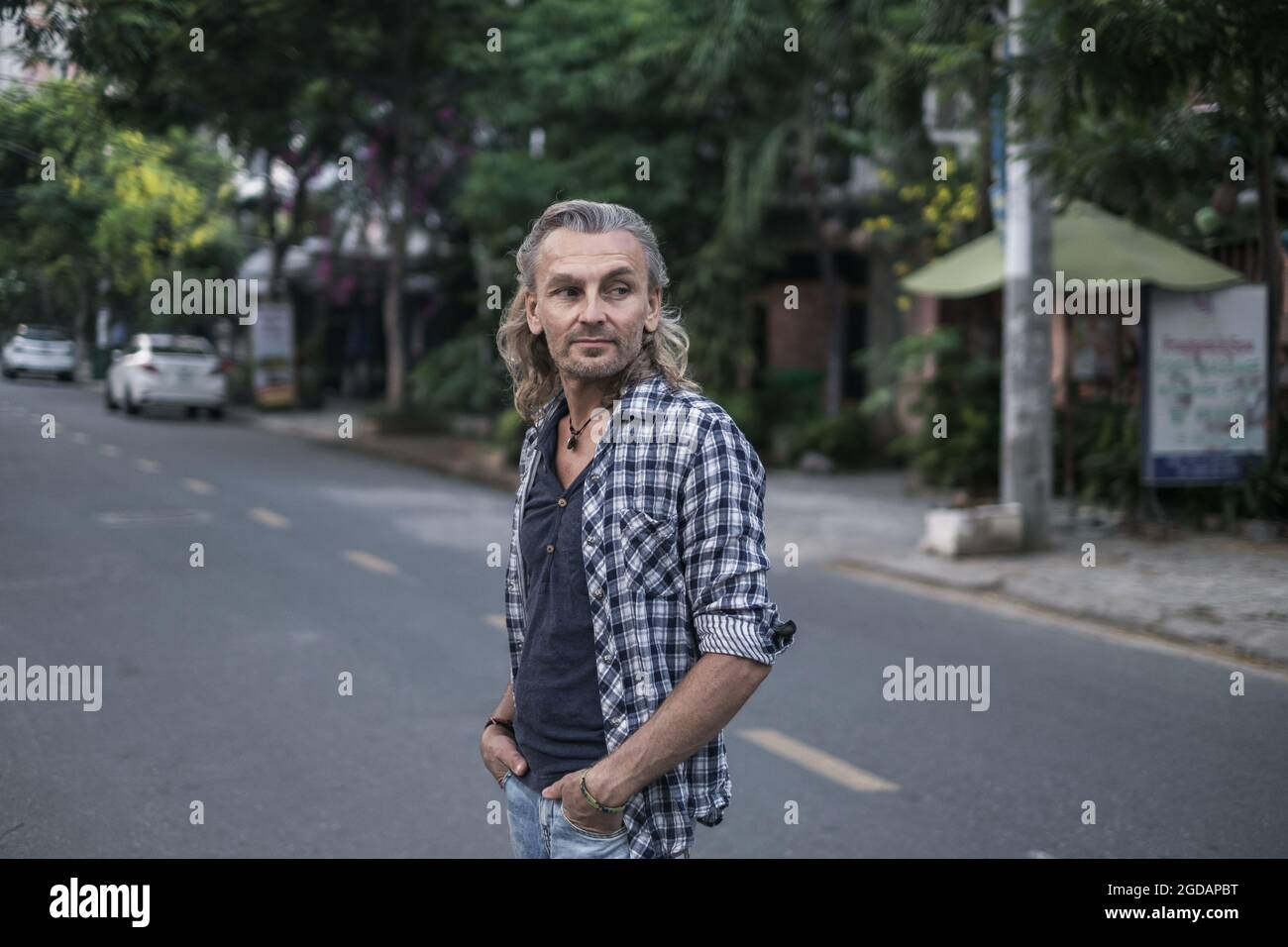 Älterer Mann im T-Shirt, Jeans, die in der asiatischen Stadt auf der Straße spazieren und seine Haare halten. Lange graue Haare. Chinesische Laternen. Hochwertige Fotos Stockfoto