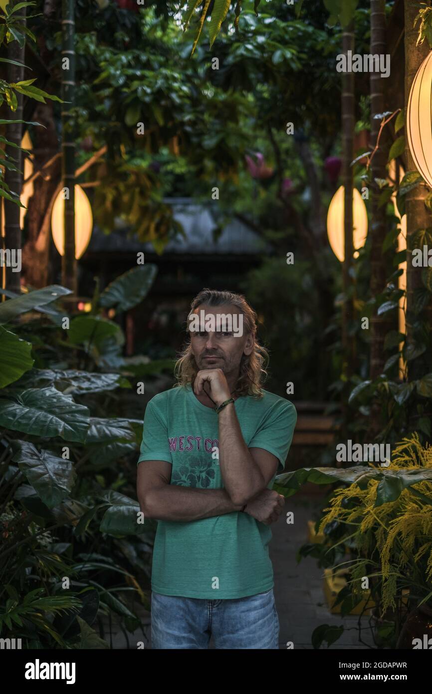 Porträt eines reifen Mannes in T-Shirt, Jeans auf der grünen Straße. Lange graue Haare. Chinesische Laternen. Hochwertige Fotos Stockfoto