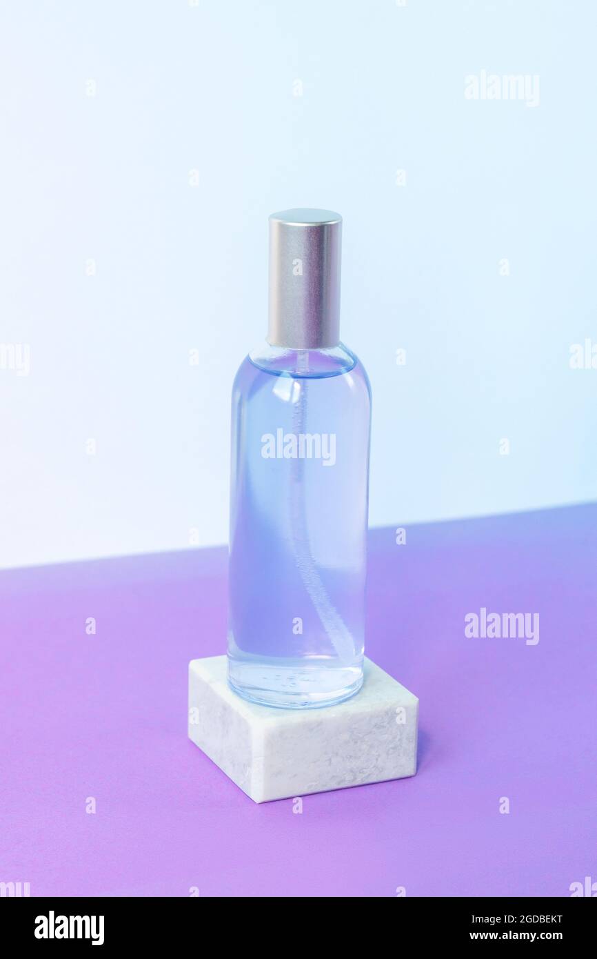 Lavendelwasser oder Hydrolat in Glasflasche auf grauem Podium auf violettem Tisch. Aromatherapie-Konzept. Modell. Stockfoto