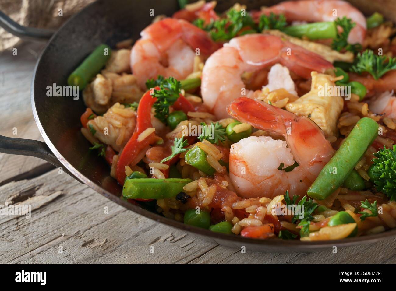 Reisgericht mit Meeresfrüchten, Huhn und Gemüse in einer Paella-Pfanne auf einem rustikalen Holztisch, Nahaufnahme, ausgewählter Fokus, enge Schärfentiefe Stockfoto