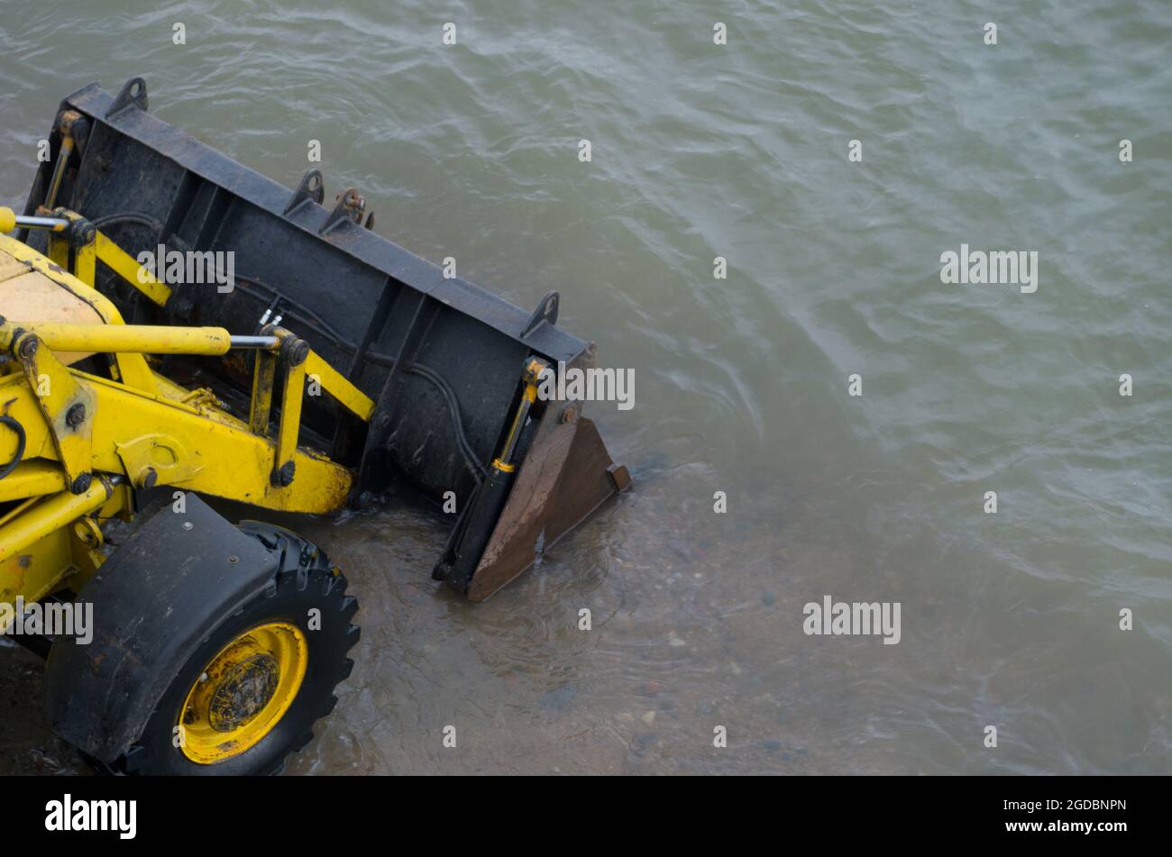 Gelbe Bulldozer mit einem Radantrieb absenkende schwarze Metallklinge, fuhr in das Meer in der Küstenzone von seichtem Wasser. Konzept: Verwendung schwerer Konstruktion Stockfoto