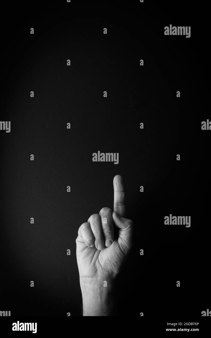 Dramatisches Schwarz-Weiß-Bild von männlicher Hand, das die Zeichensprache Nummer eins vor schwarzem Hintergrund mit leerem Kopieplatz für Redakteure zeigt Stockfoto