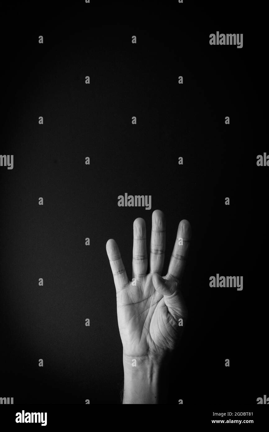 Dramatisches Schwarz-Weiß-Bild der männlichen Hand zeigt Zeichensprache Nummer vier vor schwarzem Hintergrund mit leerem Kopieplatz für Redakteure Stockfoto