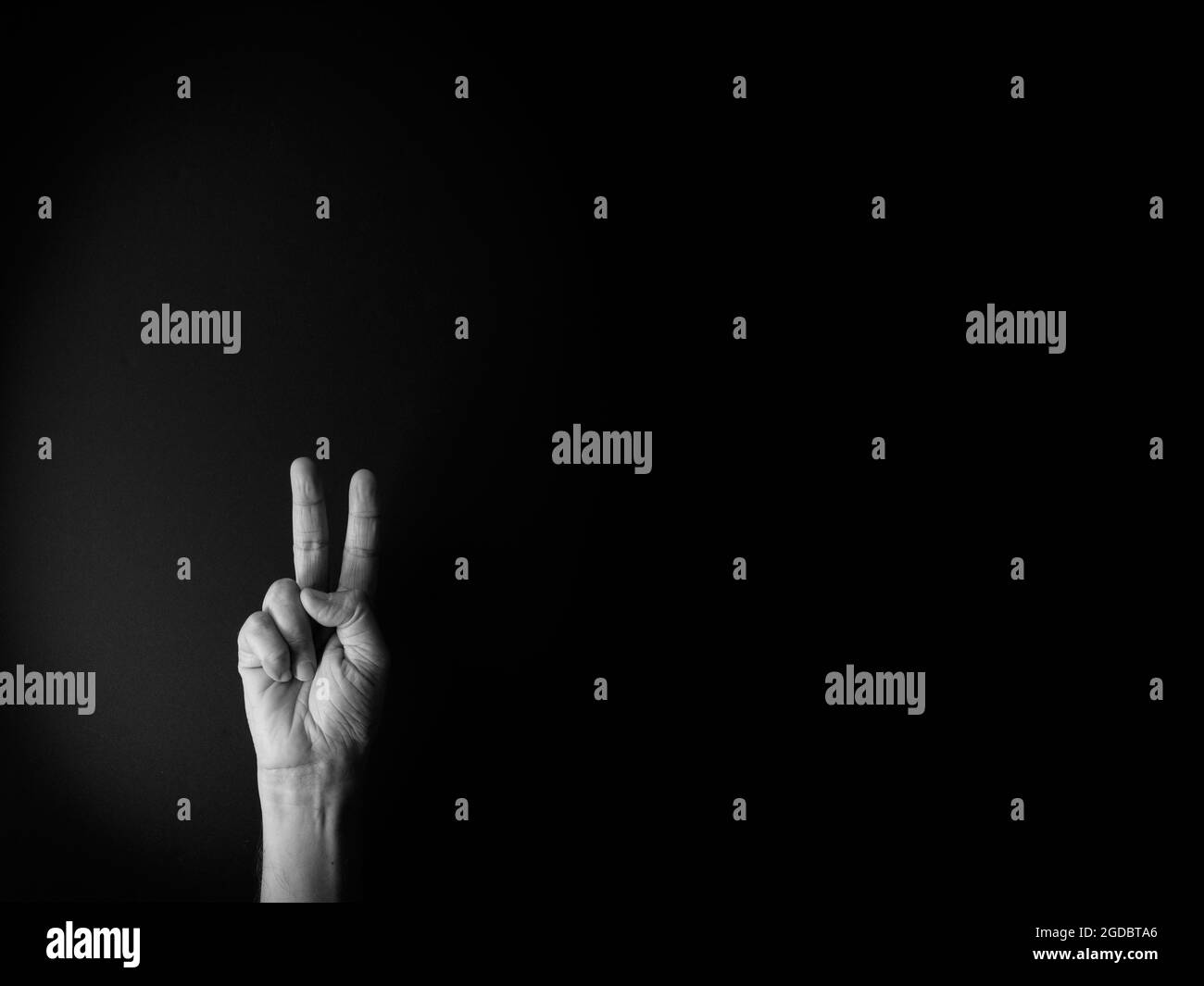 Dramatisches Schwarz-Weiß-Bild der männlichen Hand zeigt Zeichensprache Nummer zwei vor schwarzem Hintergrund mit leerem Kopieplatz für Redakteure Stockfoto