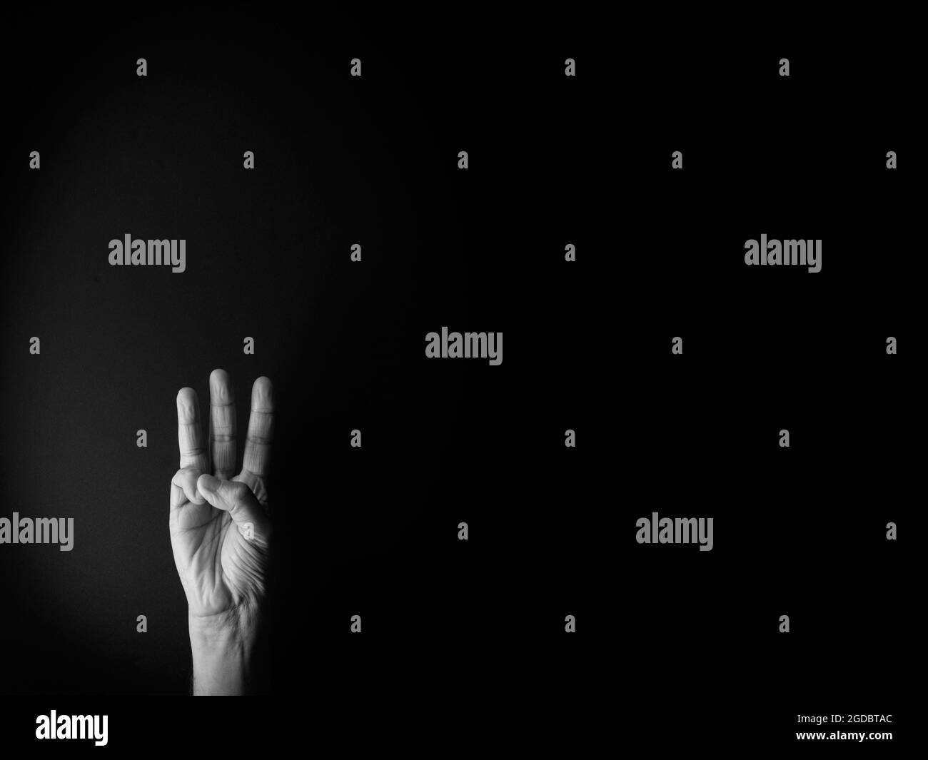 Dramatisches Schwarz-Weiß-Bild der männlichen Hand zeigt Zeichensprache Nummer drei vor schwarzem Hintergrund mit leerem Kopieplatz für Redakteure Stockfoto