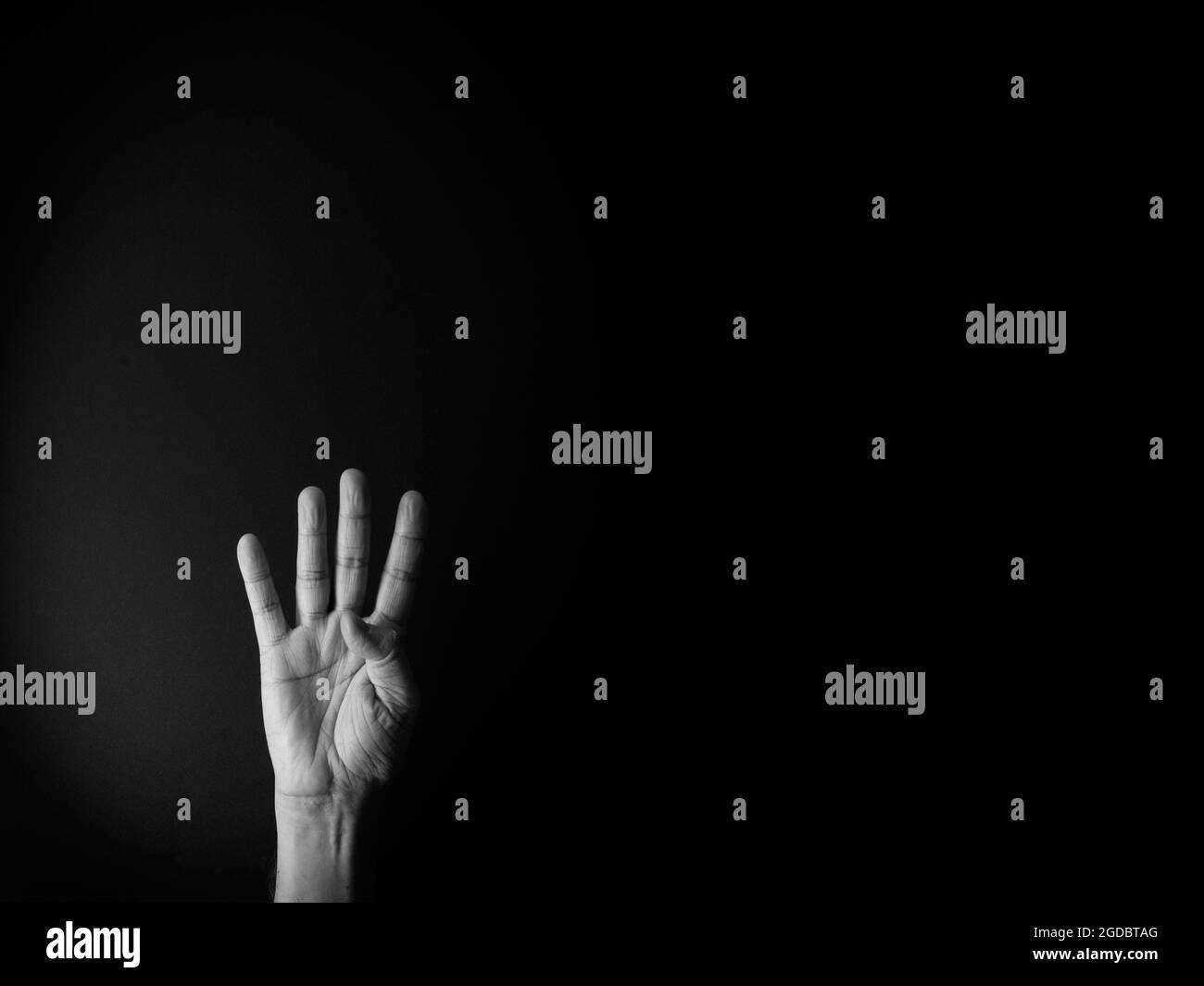Dramatisches Schwarz-Weiß-Bild der männlichen Hand zeigt Zeichensprache Nummer vier vor schwarzem Hintergrund mit leerem Kopieplatz für Redakteure Stockfoto