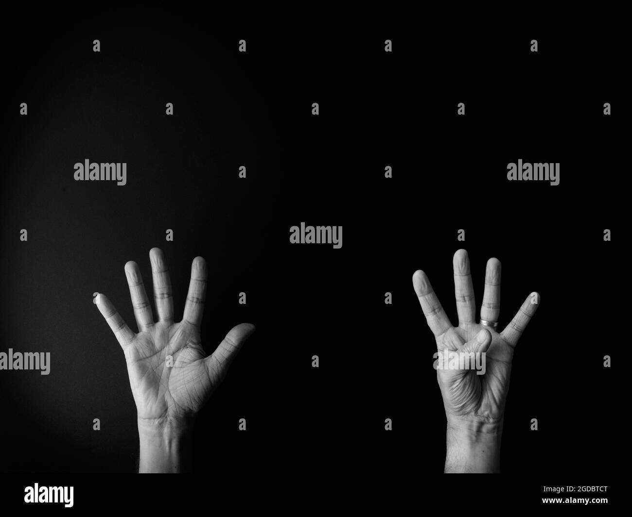 Dramatisches Schwarz-Weiß-Bild der männlichen Hand zeigt Zeichensprache Nummer neun vor schwarzem Hintergrund mit leerem Kopieplatz für Redakteure Stockfoto