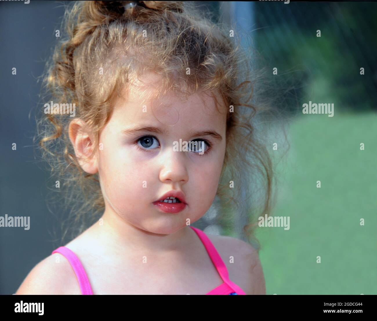 Das kleine Mädchen mit lockigen Köpfen blickt feierlich auf die Kamera. Nahaufnahme zeigt ihr kleines Mädchen Locken und Rosenknospen Mund. Stockfoto