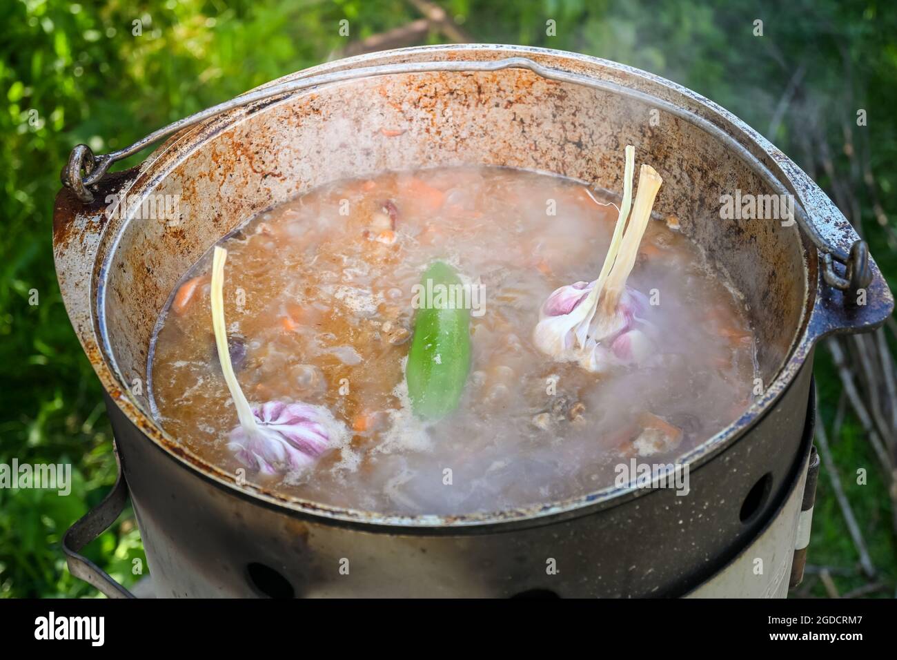 Paprika und Knoblauchköpfe in kochendem Wasser und bedecken in Scheiben geschnittene Karotten und Fleischstücke in einem Kessel, während Pilaf auf einer Traditiona gekocht wird Stockfoto