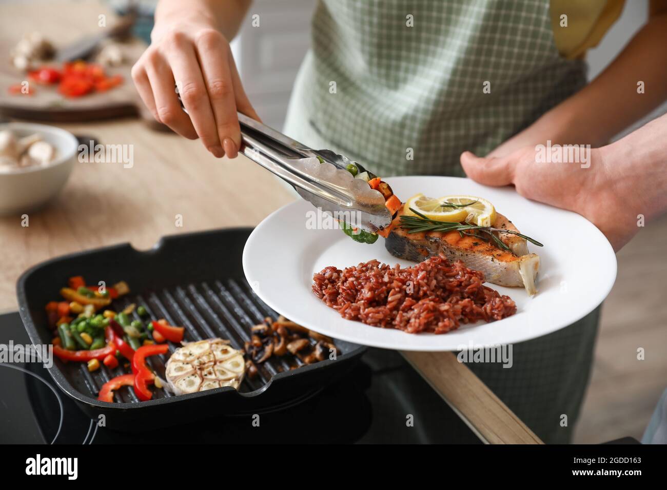 Frau, die in der Küche leckeres Gemüse mit Fisch und Reis auf den Teller legt Stockfoto