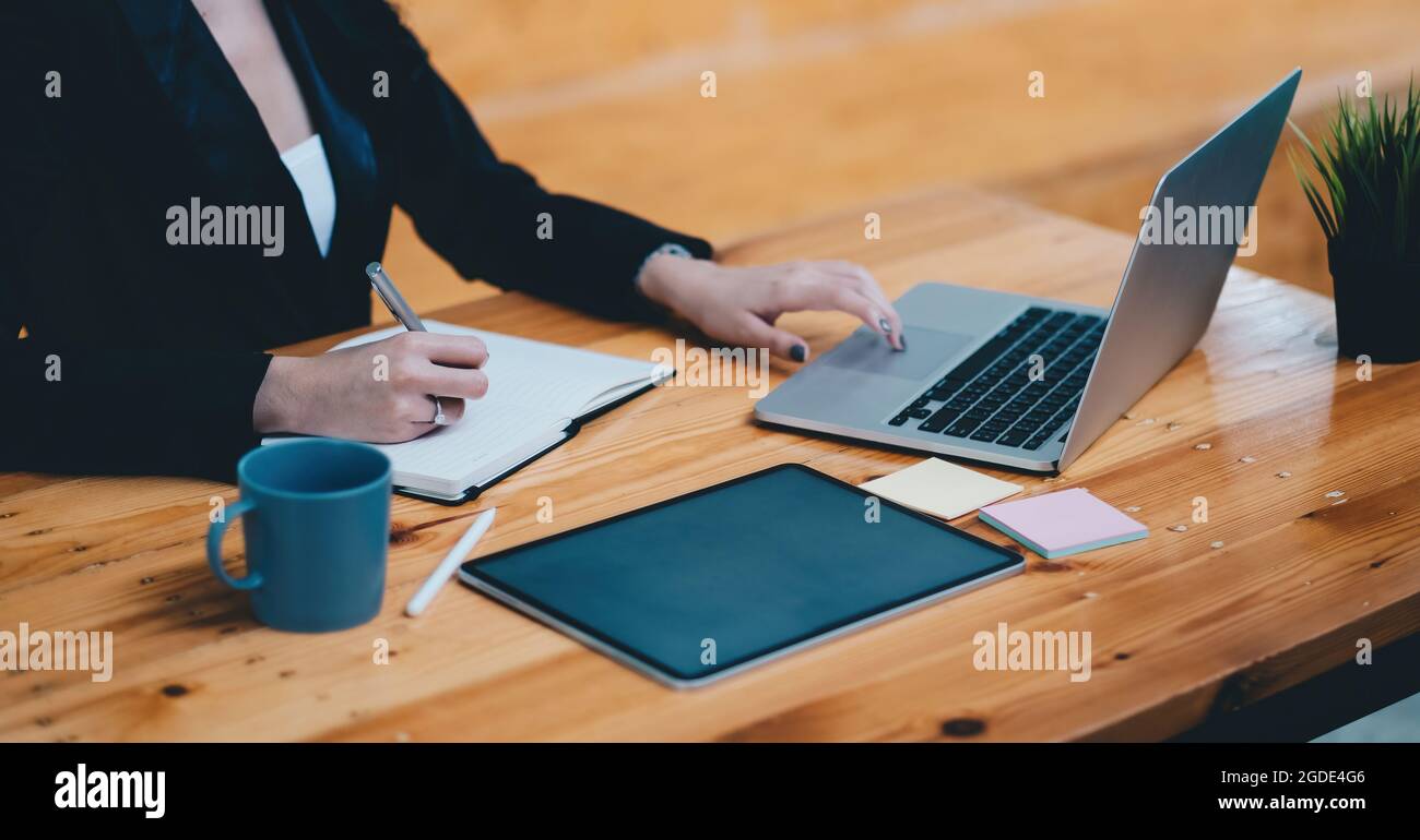 Nahaufnahme einer Frau, die sich Notizen mit verschiedenen Gegenständen auf dem Bürotisch gemacht hat. Geschäftsfrau, die mit einem Laptop arbeitet. Stockfoto