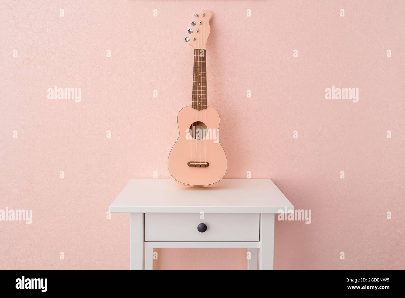 Pinke Ukulele an der rosa Wand auf dem Nachttisch Stockfoto