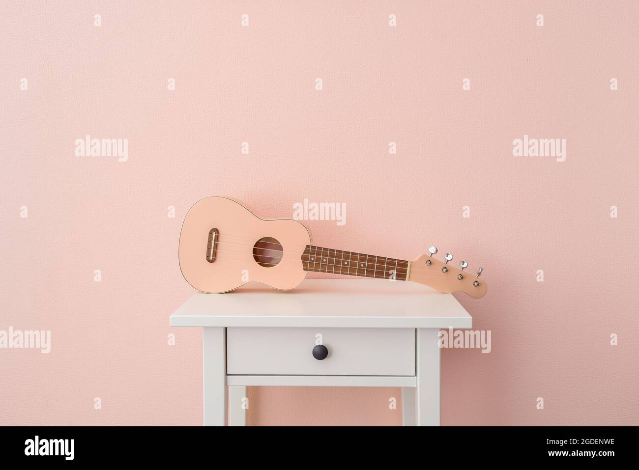 Pinke Ukulele an der rosa Wand auf dem Nachttisch Stockfoto