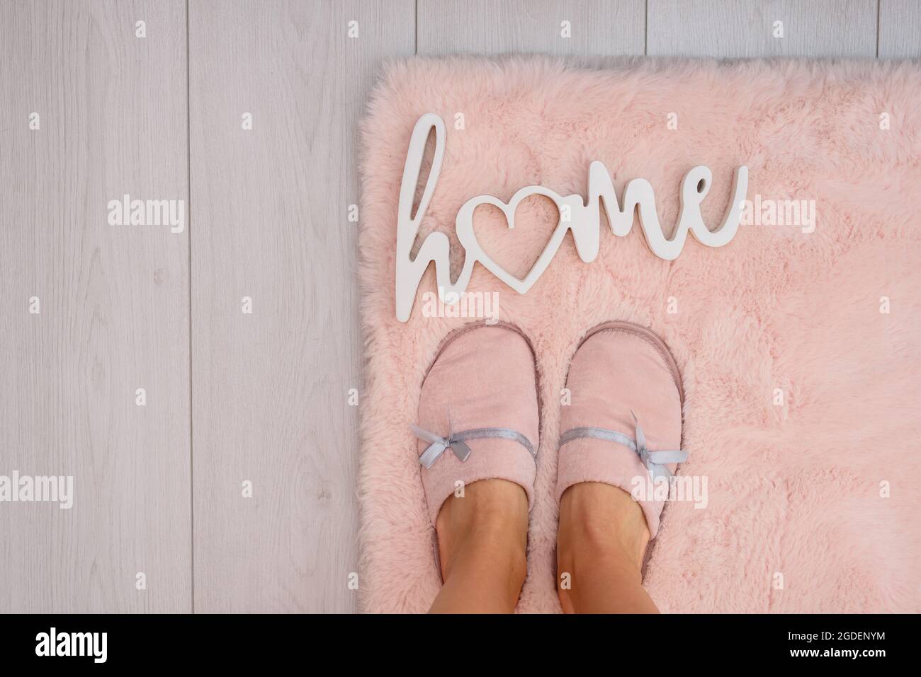 Beine in rosa Pantoffeln auf Pelzteppich und weißem Boden mit Wort ZU HAUSE Stockfoto