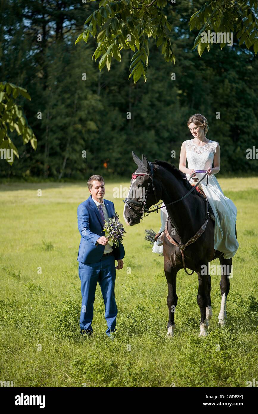 Hochzeits-Porträt im Freien. Die schöne attraktive Braut befreit das Pferd, während ihr Geliebter in der Nähe läuft. Stockfoto