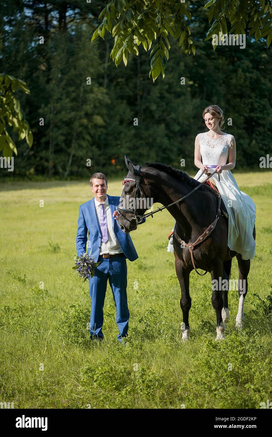 Hochzeits-Porträt im Freien. Die schöne attraktive Braut befreit das Pferd, während ihr Geliebter in der Nähe läuft. Stockfoto