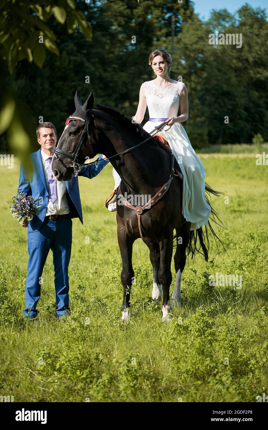 Hochzeits-Porträt im Freien. Die schöne attraktive Braut befreit das Pferd, während ihr Geliebter in der Nähe läuft. Stockfoto