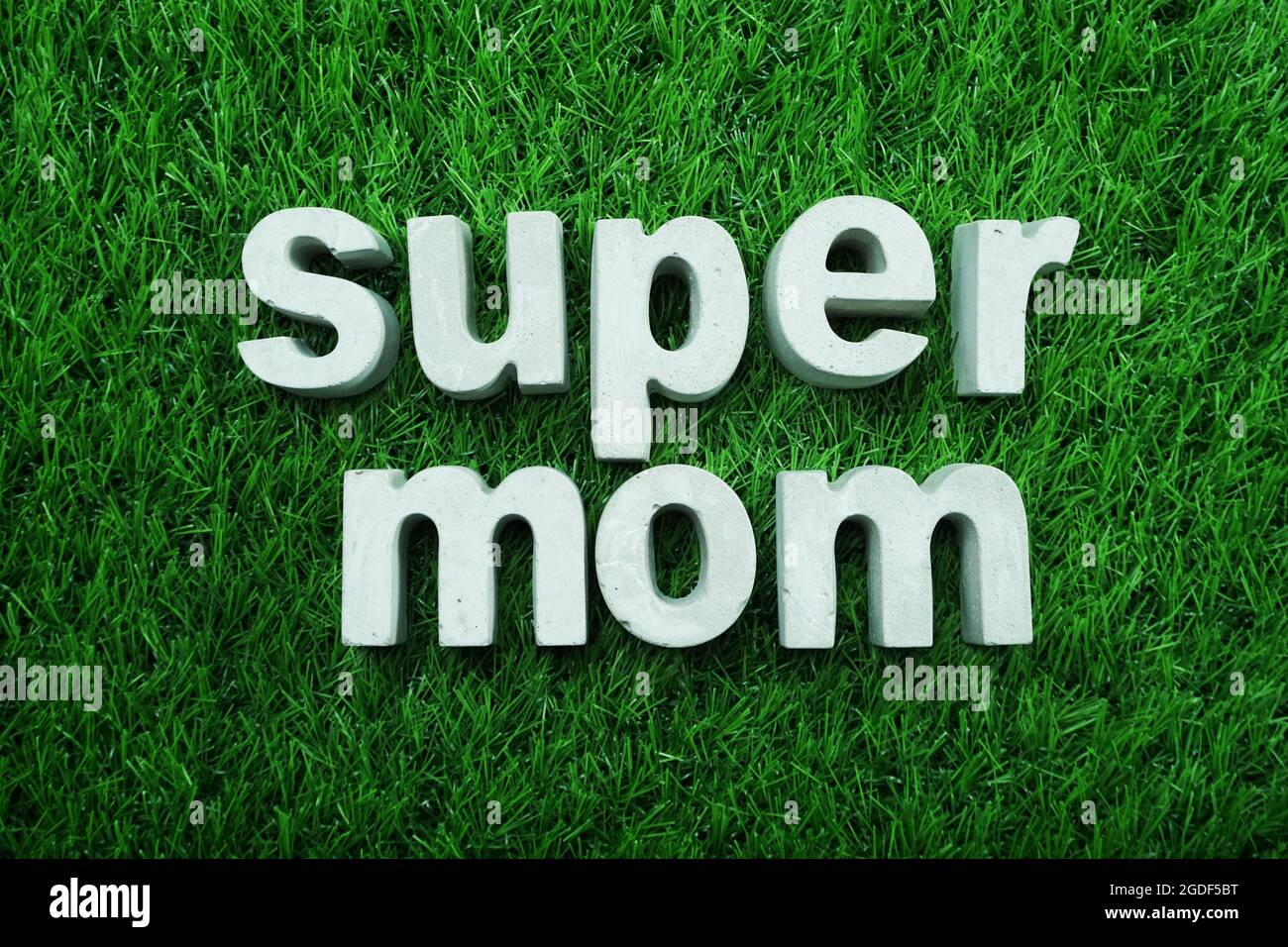 Super Mom aus Beton, Alphabet, Draufsicht auf grünem Gras Stockfoto