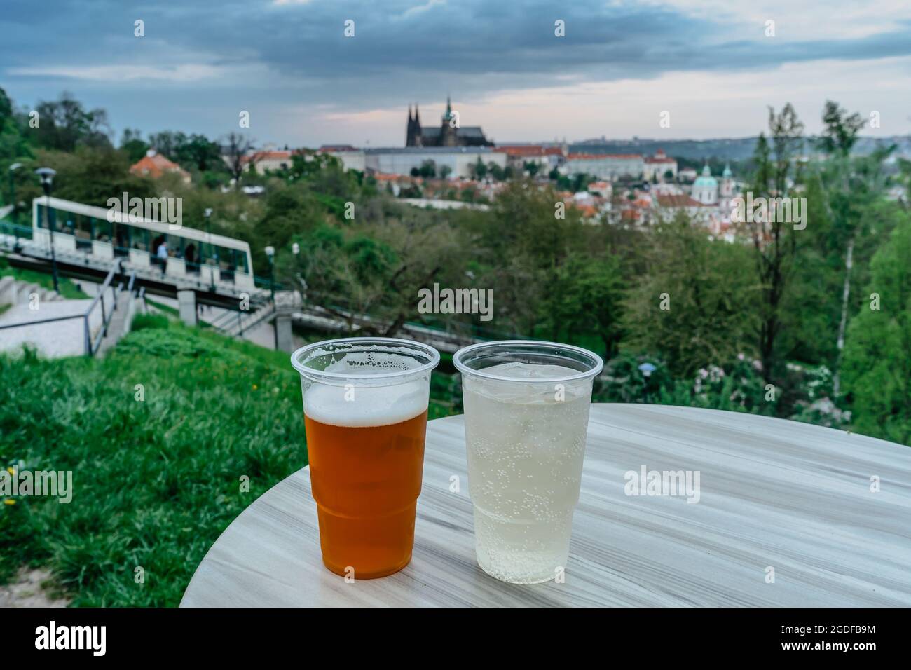 Traditionelles tschechisches Lagerbier vom Fass und Weißwein in Plastikbechern, verschwommenes Prager Schloss und Petrin-Standseilbahn im Hintergrund. Kalte Erfrischung Stockfoto