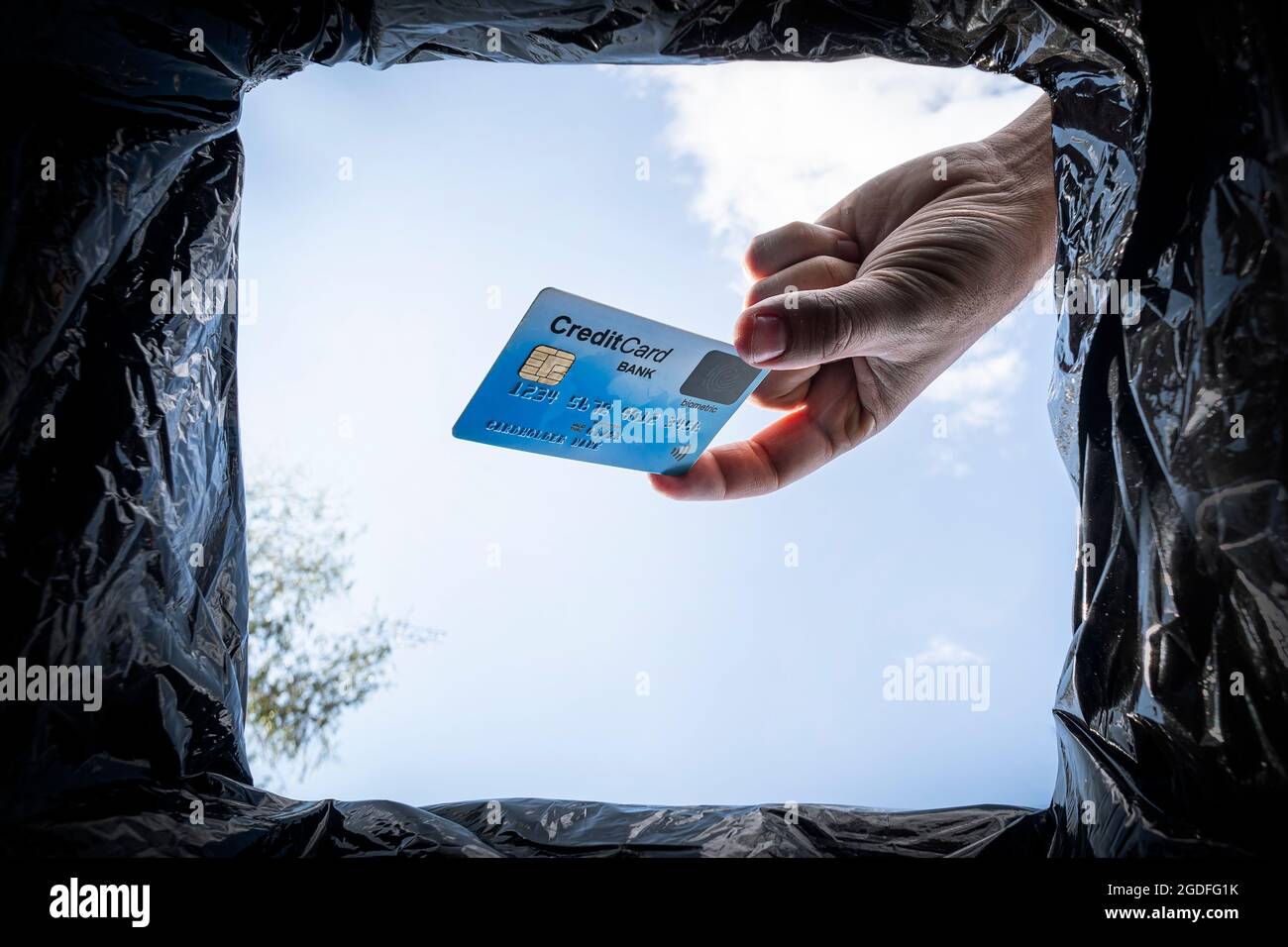 Hand wirft Kreditkarte in den Papierkorb mit Paket auf blauem Hintergrund, Ansicht unten. Das Konzept der Aufgabe von Bankgeschäften und Finanzdarlehen. Stockfoto