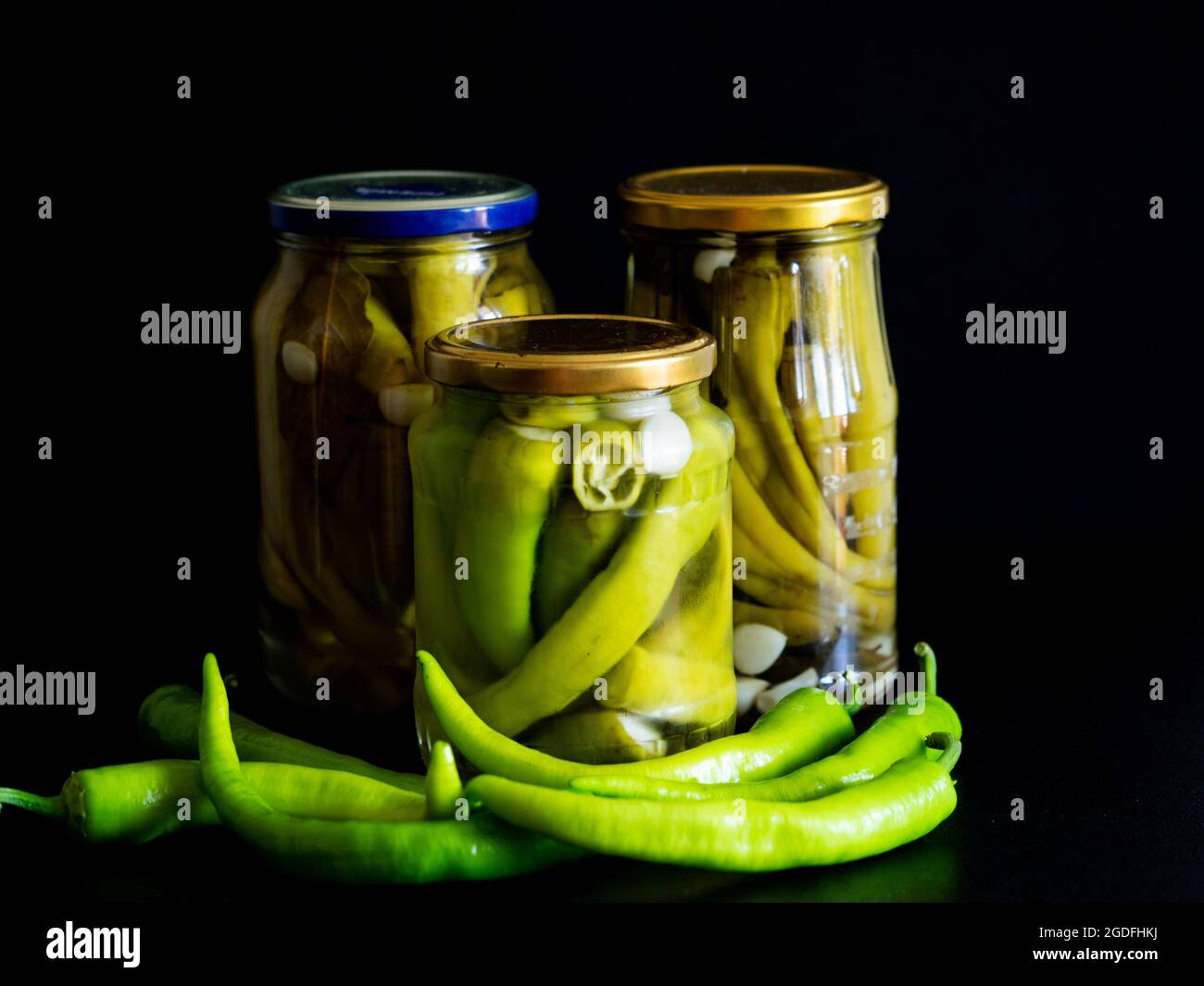 In dieser Fototafel, hausgemachte eingelegte Chilischoten in Gläsern auf schwarzem Hintergrund Stockfoto
