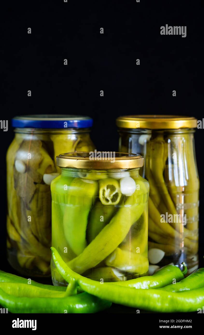 In dieser Fototafel, hausgemachte eingelegte Chilischoten in Gläsern auf schwarzem Hintergrund Stockfoto