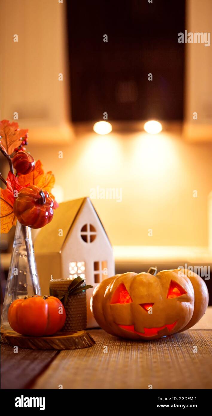 Küchendekoration für Halloween und Herbst - leuchtendes Papphaus, Kerze, Blumenstrauß mit Herbstblättern, Kakimmon, Jack-o-Laterne. Stockfoto