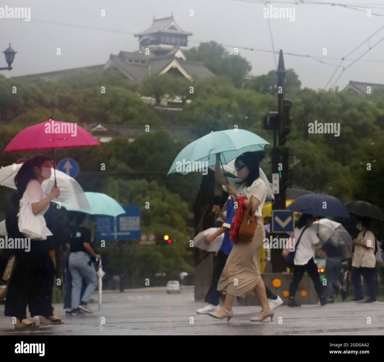 Saga, Japan, 13. August 2021.Menschen, die Regenschirme halten, gehen am 13. August 2021 im Regen in Kumamoto, im Südwesten Japans, mit Kumamoto Castle im Hintergrund. Das japanische Wetterbüro gab Warnungen für weite Gebiete des Landes aus. (Kyodo)==Kyodo Foto via Credit: Newscom/Alamy Live News Stockfoto