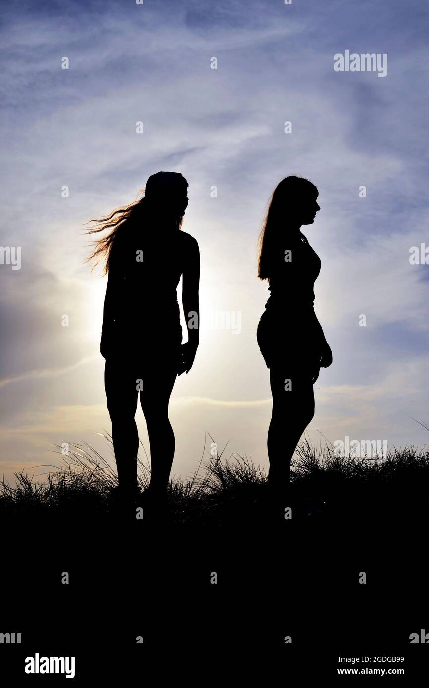 Zwei junge Frauen stehen gegen die untergehende Sonne und schauen zur Seite. Stockfoto