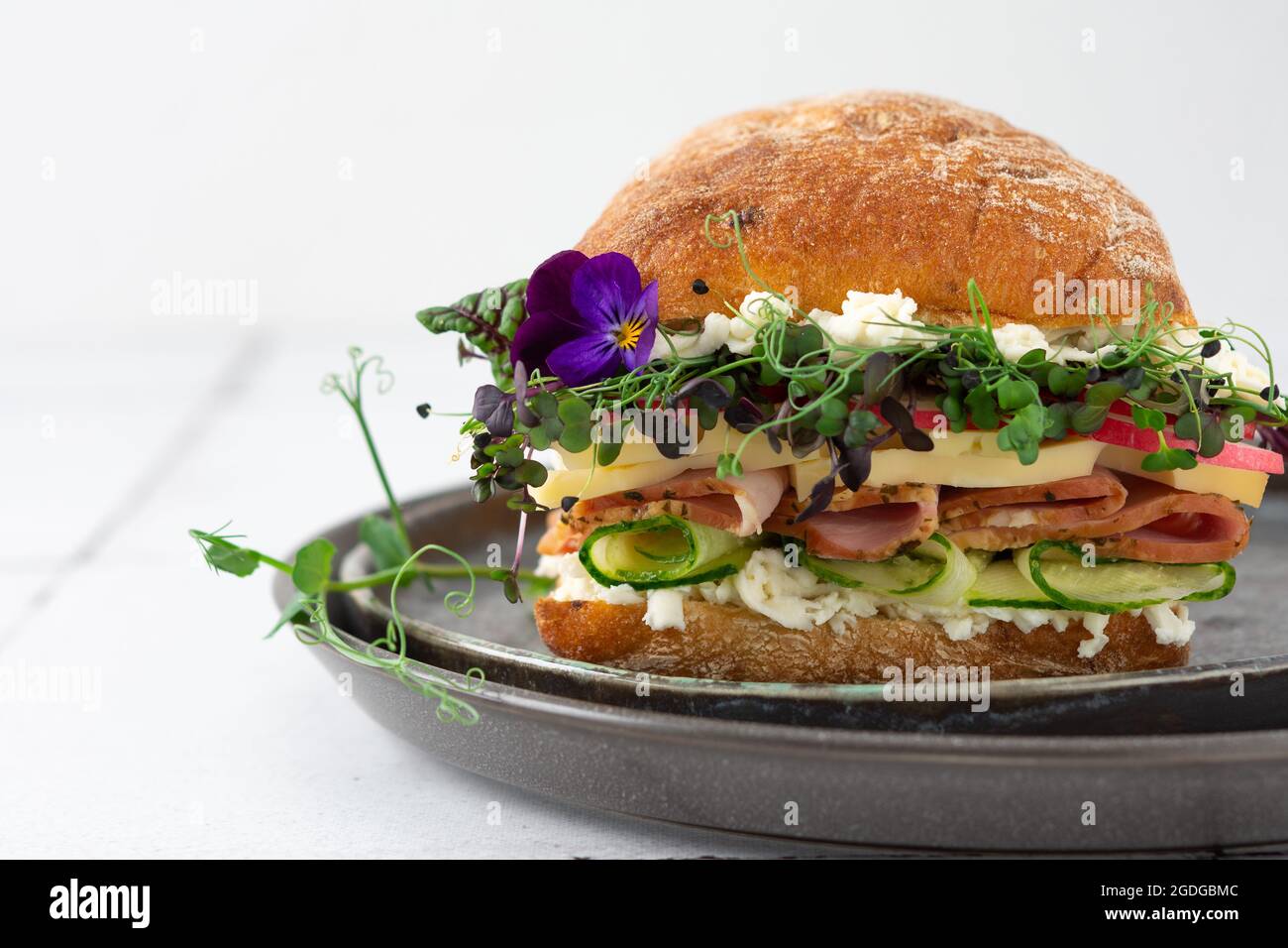 Brötchen mit Wurst, Käse und Gurken, Microgreens und Mozzarella und Radieschen, köstlicher herzhafter Burger aus nächster Nähe auf einem zu Hause gekochten Teller Stockfoto
