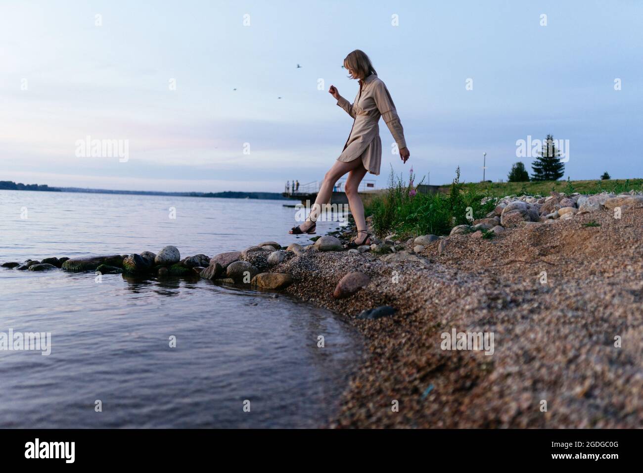 Frau am Ufer des Sees in einem Sommerkleid, tritt auf die Steine Stockfoto
