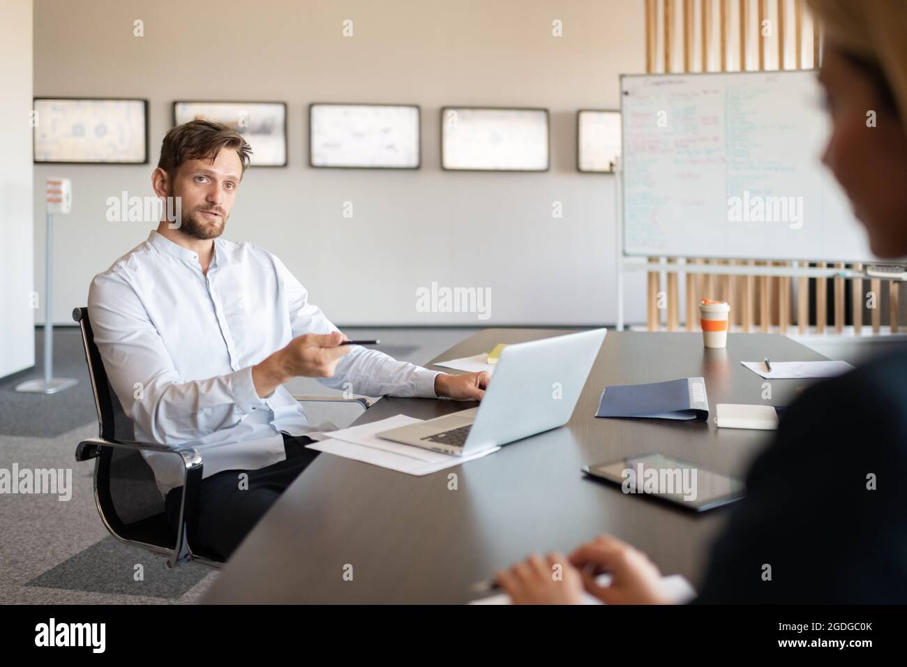 Erwachsener männlicher Chef mit Laptop, der am Tisch sitzt und im Büro mit dem neuen Rekruten spricht Stockfoto